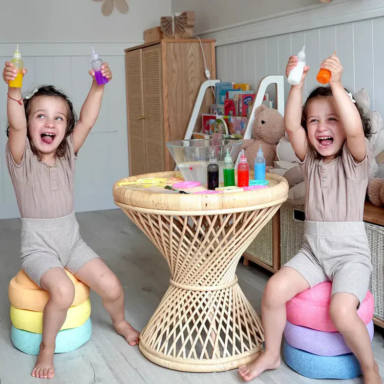 Two young children sit on cushions around a wicker table, smiling as they use Toyfettis Magic Water Wonder Kit – Create Colorful 3D Animals with Just Water, enjoying hands-on sensory fun with squeeze bottles and a mixing bowl.