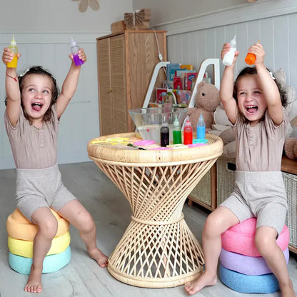 Two young children sit on cushions around a wicker table, smiling as they use Toyfettis Magic Water Wonder Kit – Create Colorful 3D Animals with Just Water, enjoying hands-on sensory fun with squeeze bottles and a mixing bowl.