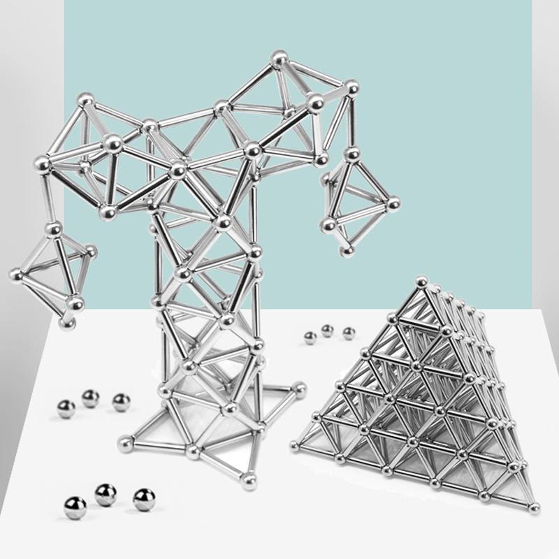 Two geometric shapes—a tree-like form and a pyramid—built with the Toyfetti MagnoCraft Magnetic Building Set rest on a white surface with scattered balls, inspiring focus, logic, and imagination against a light blue and white background.