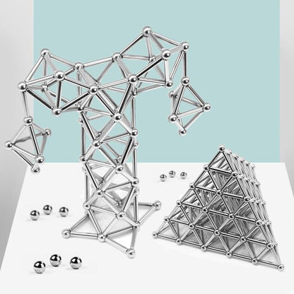 Two geometric shapes—a tree-like form and a pyramid—built with the Toyfetti MagnoCraft Magnetic Building Set rest on a white surface with scattered balls, inspiring focus, logic, and imagination against a light blue and white background.
