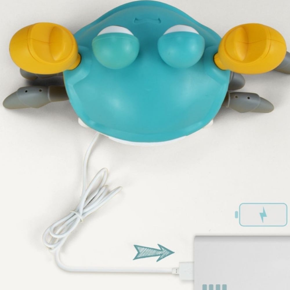 A blue and yellow Toyfetti HappyCrab – Crawling Companion with Lights & Music is connected to a white charging cable plugged into power, as an arrow and battery charging icon appear at the bottom right.