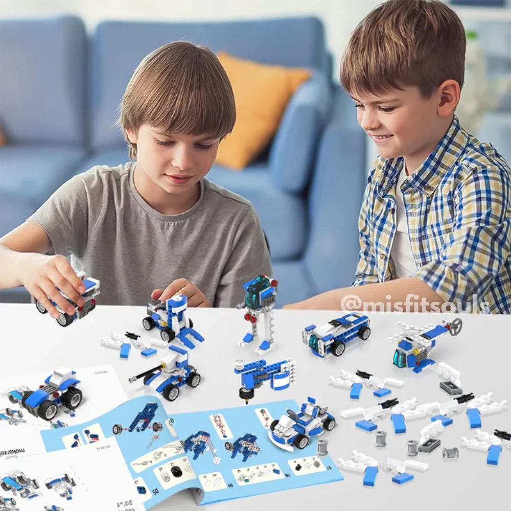 Two children sit at a table building blue and white vehicles with the Toyfetti Misfit BuildMaster 30-in-1 STEM Building Blocks Set (150+ pieces); completed models and instructions are spread out before them.