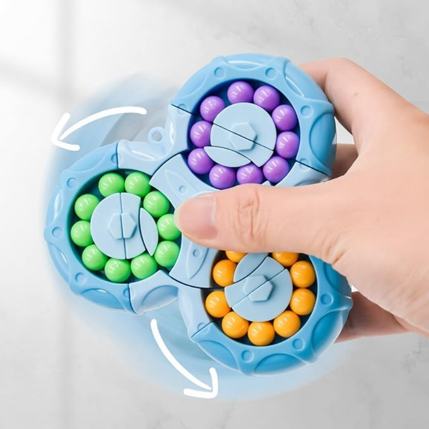 A hand spins the Toyfetti BrainBounce Rotating Logic Spinner—a blue 2-in-1 focus toy and puzzle game with three circular tracks of green, yellow, and purple beads. White arrows highlight its spinning motion on a light surface.