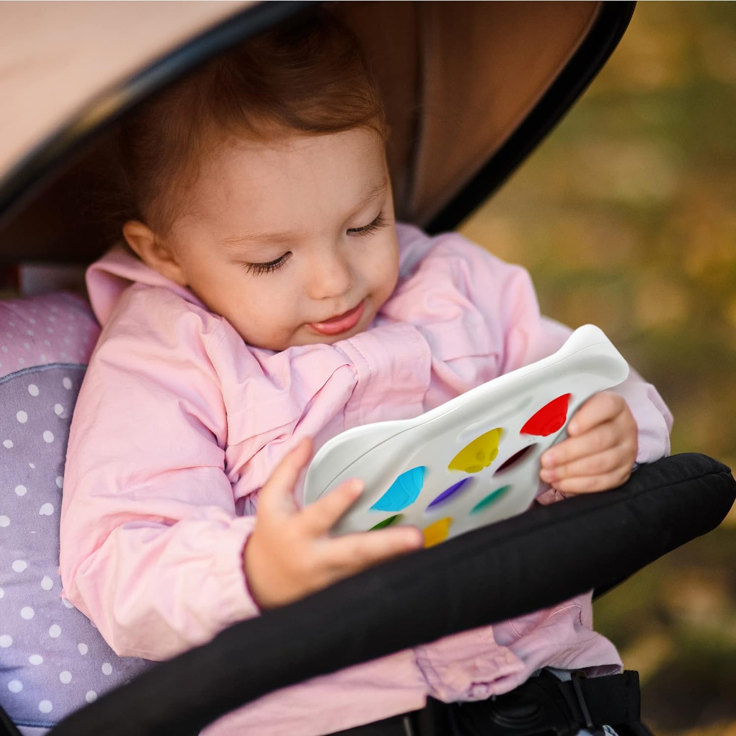 A toddler in a pink jacket sits in a stroller, happily playing with Toyfettis Press & Learn Pop Toy – Sensory Bubble Fidget for Counting & Calm, featuring colorful shapes for interactive sensory fun.