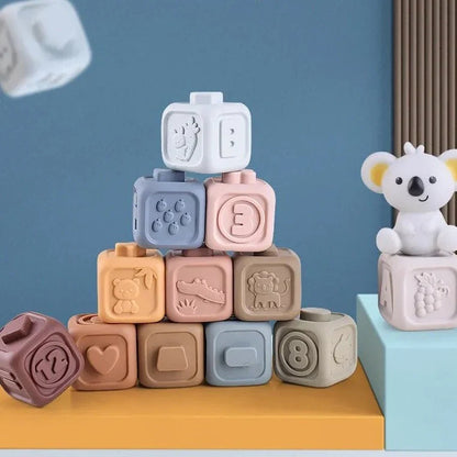 The Toyfetti CubbyKoala – Soft Silicone Teether & Stacking Toy Set for Babies features colorful, embossed animal and fruit blocks stacked on a table beside a small toy koala, set against a blue wall background.