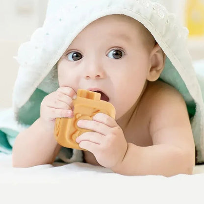 A baby lies on its stomach under a towel, chewing on a Toyfetti CubbyKoala Soft Silicone Teether & Stacking Toy Set, gazing up with wide eyes.
