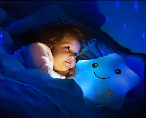 A young child cuddles the Toyfetti GlowPals Light-Up Plush Night Buddy, a blue star with a happy face that glows softly and projects stars—offering comfort and a soothing night light for kids at bedtime.