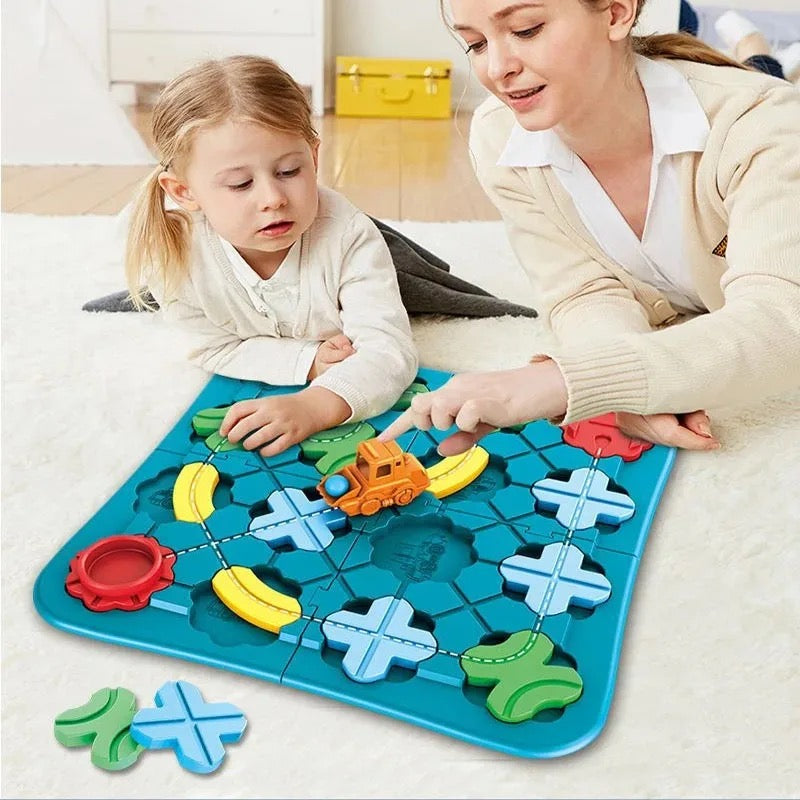 A woman and a young girl play on a white carpet with the Toyfetti Trackmaster, an interactive treinspoorset that stimulates creativity and logical thinking. Colorful pieces and gears are scattered as they move a small orange toy truck on the tracks.