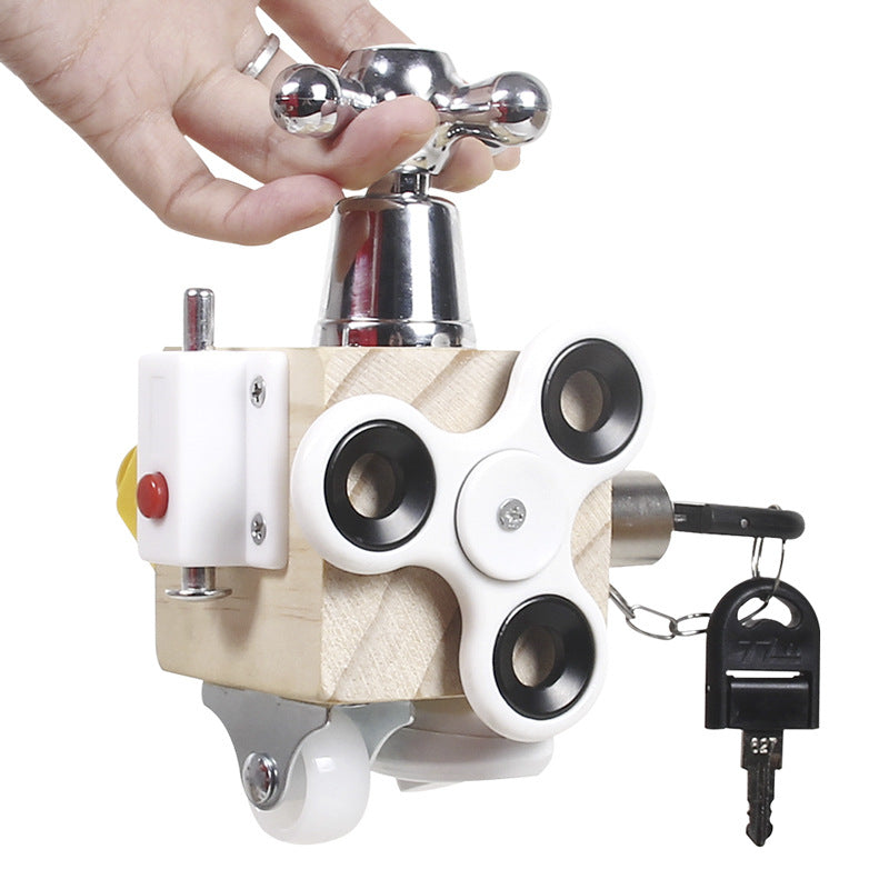 A hand holds the Toyfetti Montessori Lock & Key Learning Cube—a hands-on sensory toy with a faucet handle, fidget spinner, red button, caster wheel, and key on a chain—perfect for building kids’ fine motor skills.