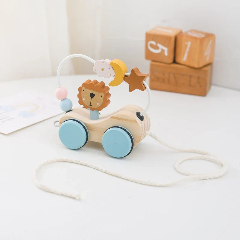 The Toyfetti Bead Tracks Wooden Maze Toy features blue wheels, a lion face, colorful wire beads for hand-eye coordination, and a white pull string. Wooden number blocks appear in the background. Perfect for early motor skill development.