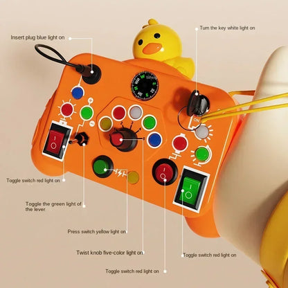 The Toyfetti BusyBoard Logic & Light Panel is an orange sensory switch board with labeled buttons and knobs for hands-on play. A yellow rubber duck on the top right adds a playful, Montessori-inspired detail.