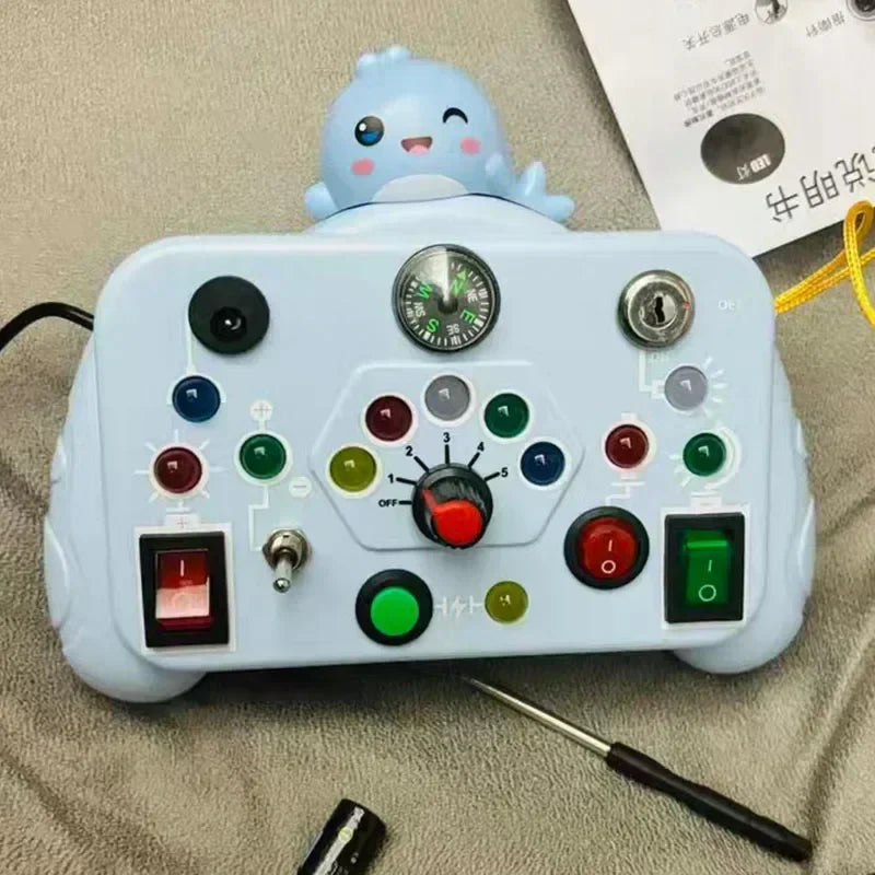 The Toyfetti BusyBoard Logic & Light Panel is a Montessori-inspired switch board in light blue with colorful buttons, a knob, switches, compass, and a cute dinosaur figure—perfect for sensory play. Includes screwdriver and paper.