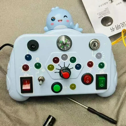 The Toyfetti BusyBoard Logic & Light Panel is a Montessori-inspired switch board in light blue with colorful buttons, a knob, switches, compass, and a cute dinosaur figure—perfect for sensory play. Includes screwdriver and paper.