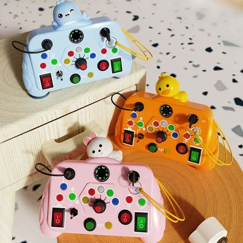 Three Toyfetti BusyBoard Logic & Light Panels, each with animal designs (blue seal, yellow duck, white bunny), rest on wood. These Montessori-inspired switch boards offer buttons, switches, and dials for engaging sensory play.