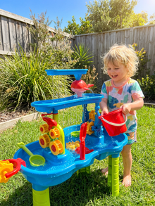 Child playing with a colorful water play set in a backyard