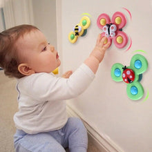 A baby in a white shirt and blue pants sits on the floor, reaching for Toyfettis Whirlie Baby Spinner – Sensory Spin Toy for Fine Motor Fun, colorful insect-themed spinners that promote sensory development as they spin on the wall.