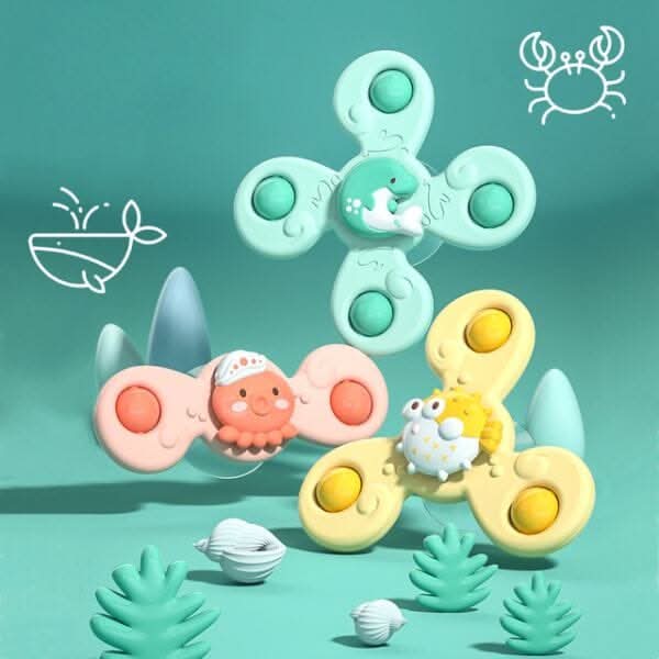 The Toyfetti Whirlie Baby Spinner features three colorful animal spinners—a seal, octopus, and crab—set among pastel plants and seashells, perfect for sensory development. Whimsical whale and crab drawings add playful charm to the scene.