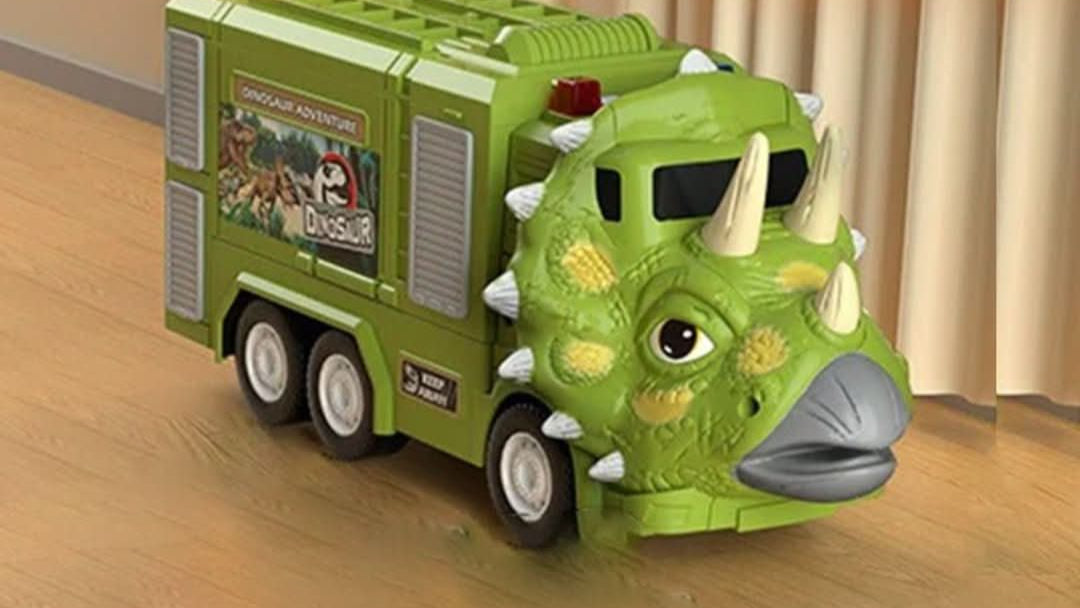 The Toyfetti DinoTransporter – T-Rex & Triceratops Truck with Lights and Sound features a green dinosaur face, horns, six wheels, and a Dinosaur Adventure sticker, perfect for interactive fun on the floor by beige curtains.