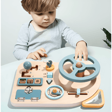 A young child explores the Toyfetti Montessori Car Press Board – Hands-On Driving Toy for Curious Toddlers, a wooden activity set with steering wheel, gear shift, switches, and dials in soft blue, ideal for building fine motor skills.