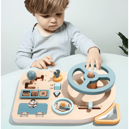 A young child explores the Toyfetti Montessori Car Press Board – Hands-On Driving Toy for Curious Toddlers, a wooden activity set with steering wheel, gear shift, switches, and dials in soft blue, ideal for building fine motor skills.
