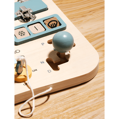 The Toyfetti Montessori Car Press Board is a hands-on driving toy for curious toddlers, featuring a blue gear shift, switches, symbols, and a yellow key on a string to develop fine motor skills on a light wood surface.