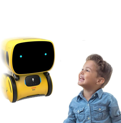 A young boy in a blue shirt smiles at the Toyfetti Robomate | Jouw Muzikale Vriend - Slimme Robot, featuring a black screen face and blue eyes, against a plain white background.