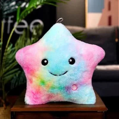 The Toyfetti GlowPals Light-Up Plush Night Buddy, a star-shaped pillow with a multicolored tie-dye pattern and a smiling face, provides comforting bedtime glow in cozy indoor spaces.
