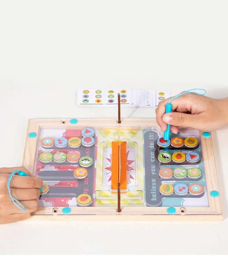Two hands play Toyfetti’s Magnetic Maze – Strategy and Coordination Game for Kids, each guiding colorful round pieces with a blue magnetic pen through patterned paths, developing fine motor skills. A symbols card sits above the board.