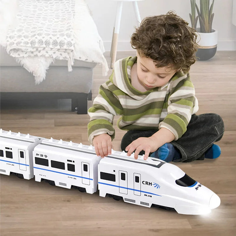 A young child with curly hair, in a green and white striped sweater, sits on a wooden floor playing with the Toyfetti GlowExpress—an obstacle-avoiding, light-up train designed for magical play and skill building—in the living room.