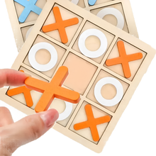 A hand places an orange X piece on the Toyfetti Wooden Tic Tac Toe for Family Fun & Home Style, with white O pieces on the board and another set in the background—ideal for game nights or stylish home décor.