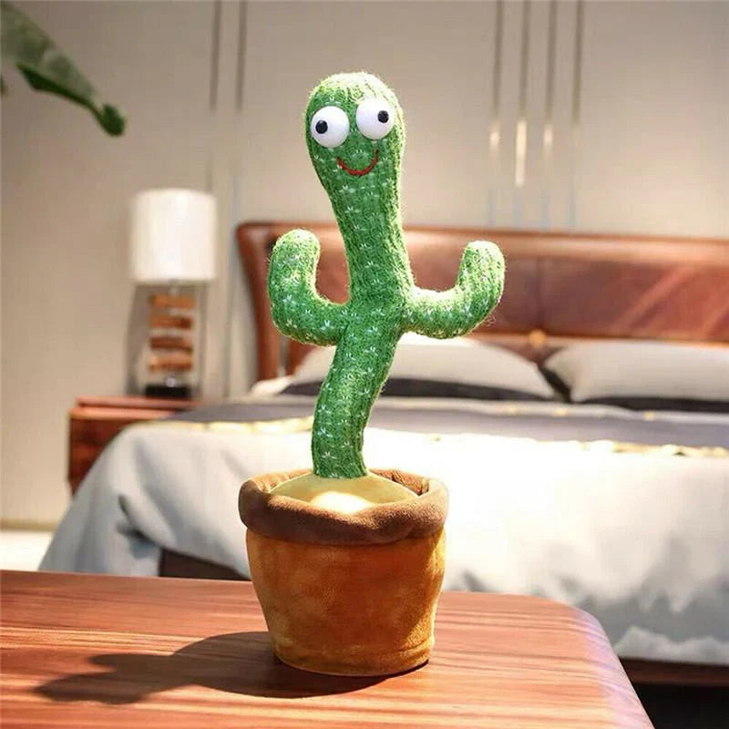 The Toyfetti CactusBuddy – Dancing Talking Plush Toy stands in a brown pot on a table in a modern bedroom, its googly eyes and smiling face adding charm near the bed and lamp. This toy keeps kids smiling and engaged.