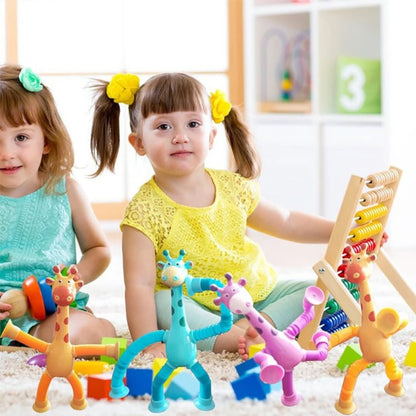 Two young girls sit smiling on the floor, playing with Toyfetti’s Stretchy Giraffe Trio—bendable sensory toys with suction cups—amid colorful building blocks and an abacus in a bright, cheerful room.