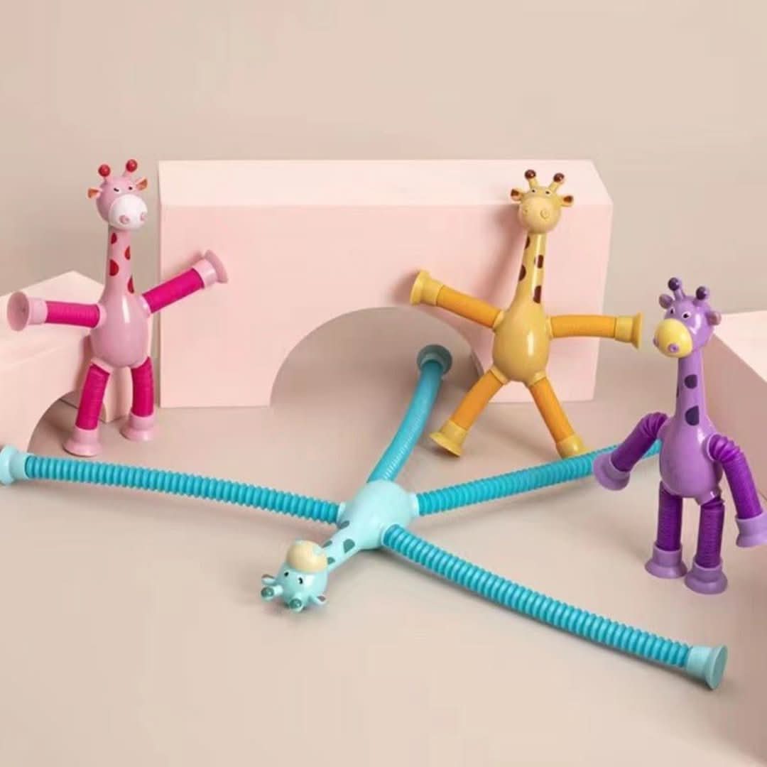 Three colorful Toyfetti Stretchy Giraffe Trio toys with bendable limbs and suction cups, in pink, yellow, and blue, are posed on a pale pink block and arch—fun cartoon-style sensory toys perfect as toddler party favors.