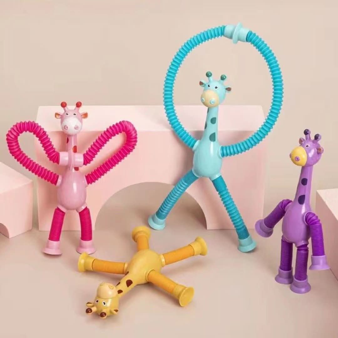 Toyfetti’s Stretchy Giraffe Trio – Bendable Sensory Toys with Suction Cups in pink, blue, and yellow are arranged on a beige surface with pink blocks. These colorful toys make perfect toddler party favors.