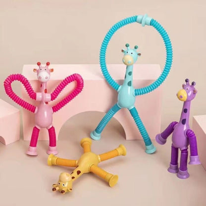 Toyfetti’s Stretchy Giraffe Trio – Bendable Sensory Toys with Suction Cups in pink, blue, and yellow are arranged on a beige surface with pink blocks. These colorful toys make perfect toddler party favors.