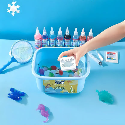 A hand dips a white crab mold from the Toyfetti Magic Water Wonder Kit – Create Colorful 3D Animals with Just Water into a blue tub, surrounded by bottles, nets, and crafting supplies on a table with colorful sea creatures and a blue backdrop.